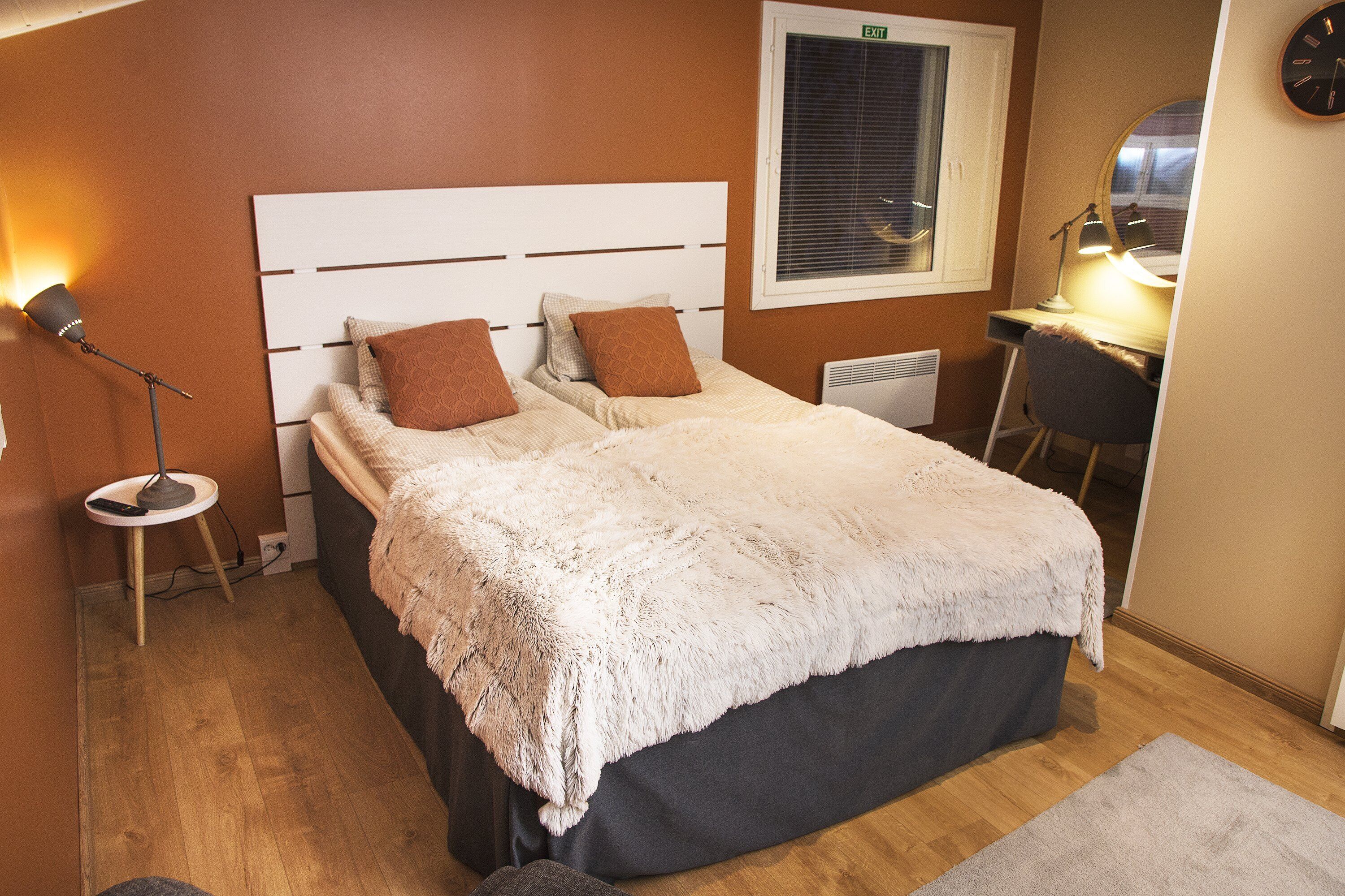 A bedroom with a bed, a desk, a chair, a lamp, and a clock on the wall.