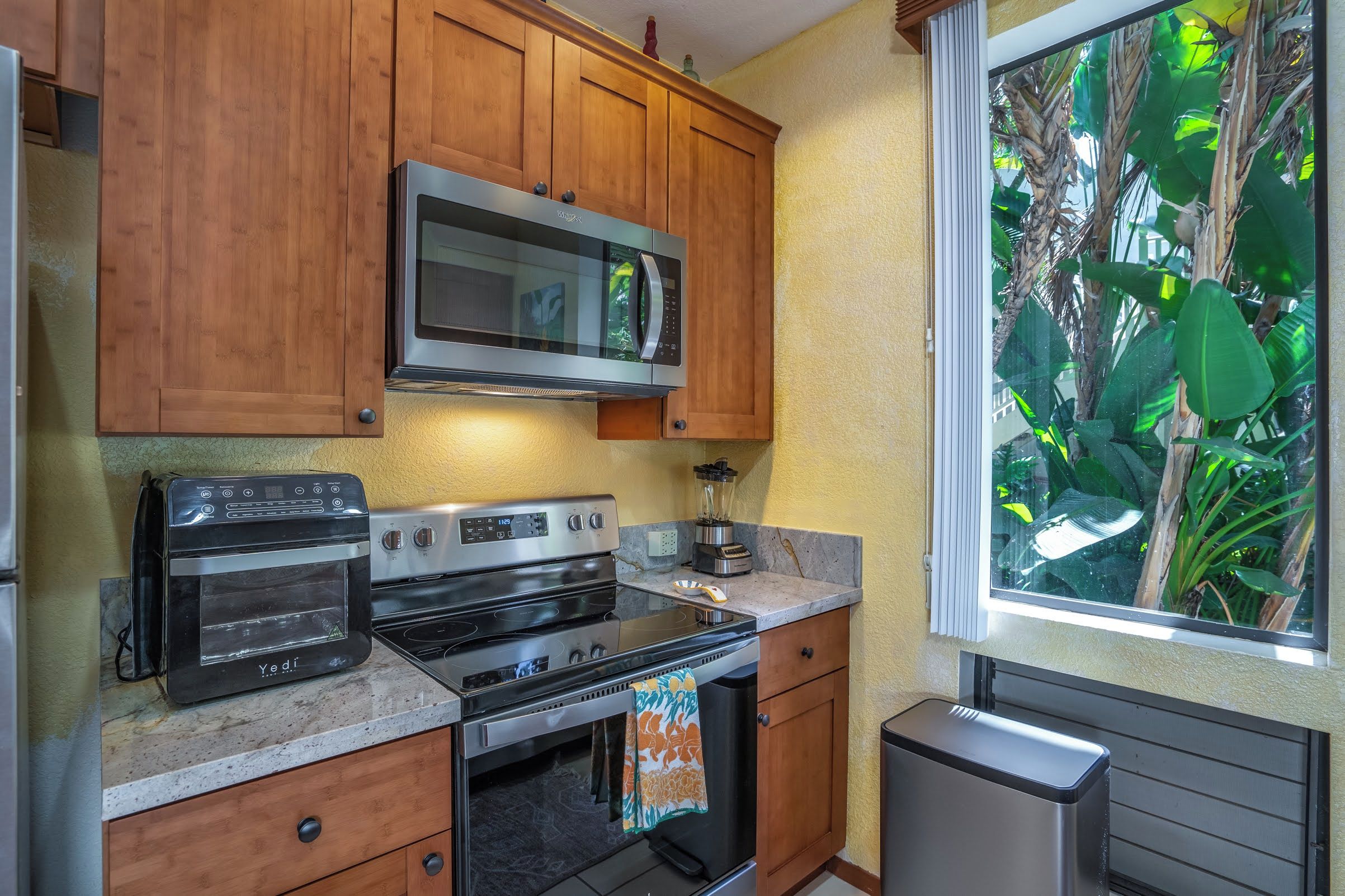 A kitchen with wooden cabinets, a microwave, a toaster, and a window with a view of greenery.
