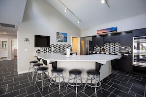 Una cocina moderna con una isla grande, salpicadero a cuadros blanco y negro, electrodomésticos de acero inoxidable y taburetes de bar.