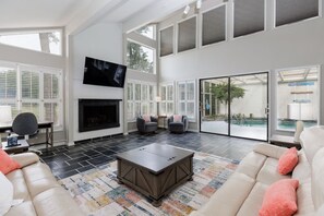 Un salón amplio con chimenea, asientos cómodos y ventanas grandes que ofrecen vistas al exterior.