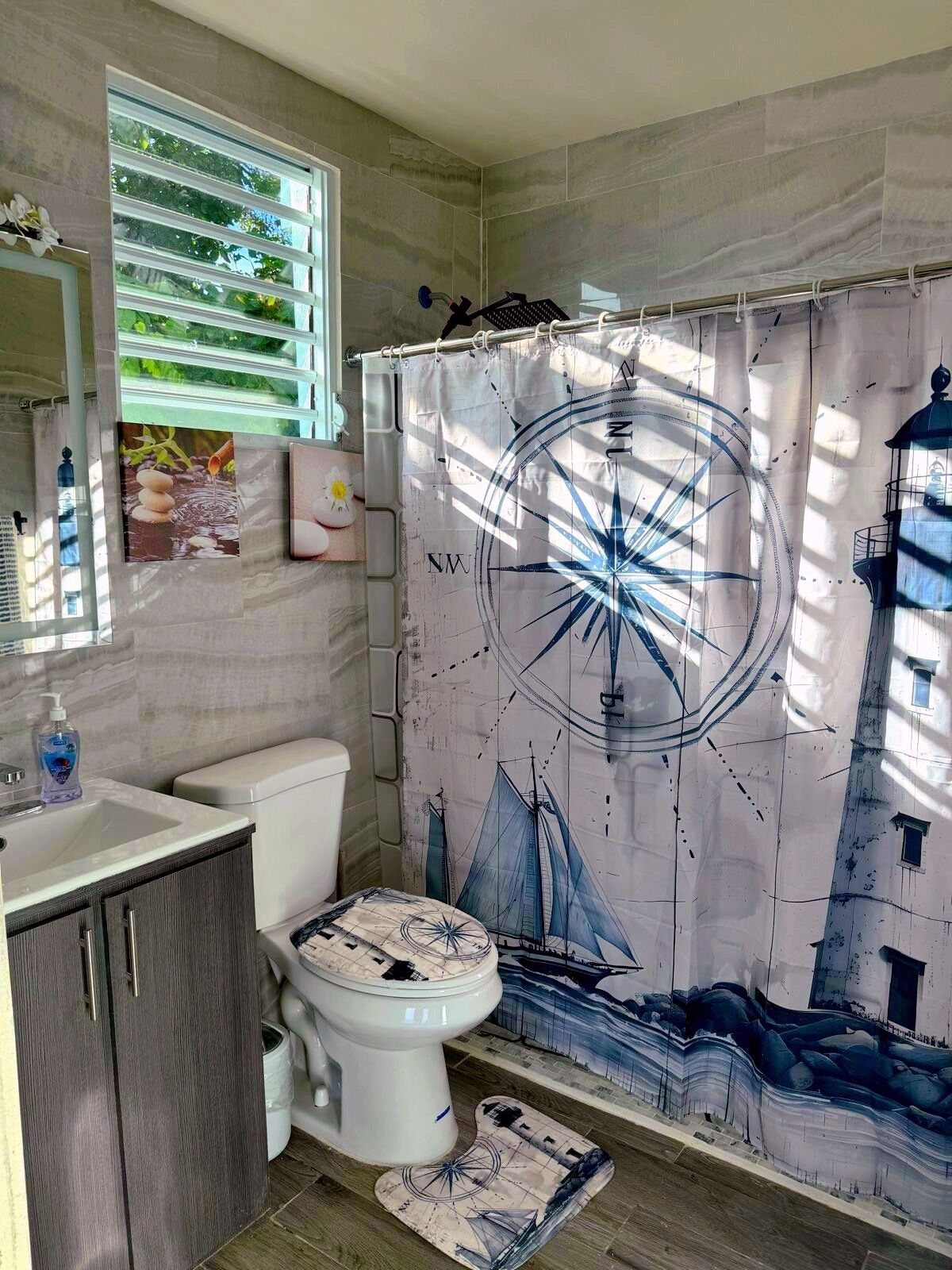 Un bagno con tenda da doccia a tema nautico, un water, un lavandino e un armadietto.