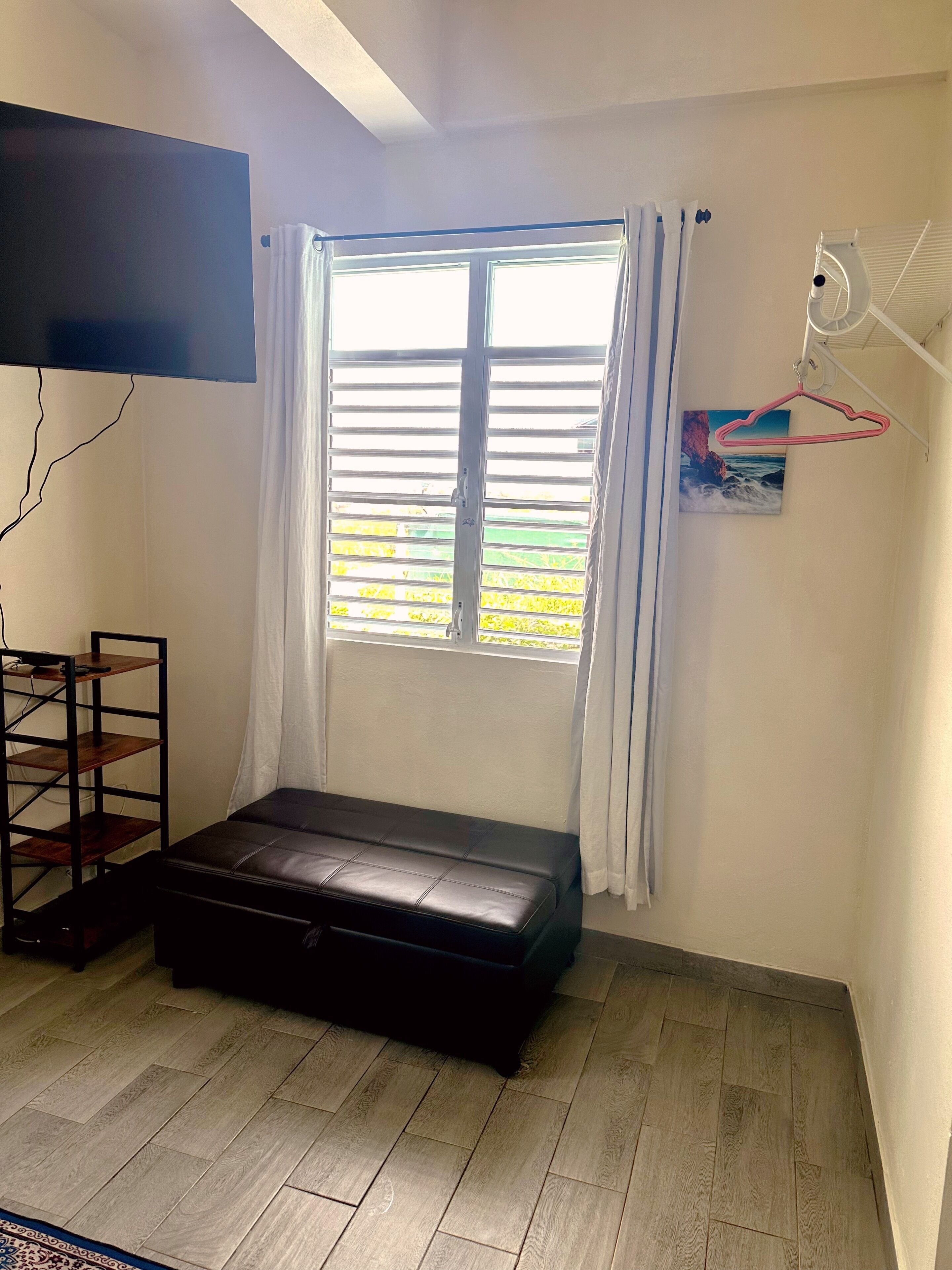 Una habitación con ventana, un banco, un televisor montado en la pared y un ventilador de techo.
