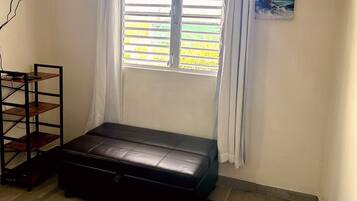 Una habitación con ventana, un banco, un televisor montado en la pared y un ventilador de techo.