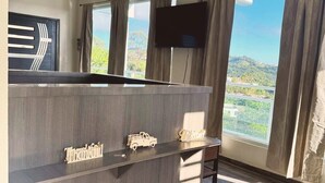 A modern room with a wooden reception desk, a flat-screen TV mounted on the wall, and large windows offering a view of a hilly landscape. - Charming house, stunning views in brilliant Barranquitas with AC, WiFi, Parking (Barranquitas)