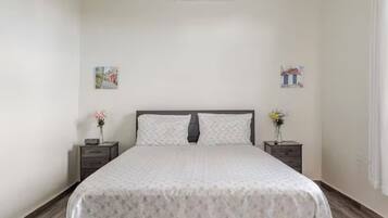 Un dormitorio ordenado con cama, mesitas de noche y adornos en la pared.
