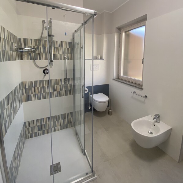 A bathroom with a glass-enclosed shower, a white sink, and a toilet. - Vatikurca (San Nicola Arcella)