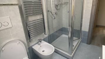 A bathroom with a toilet, bidet, and a glass-enclosed shower stall.