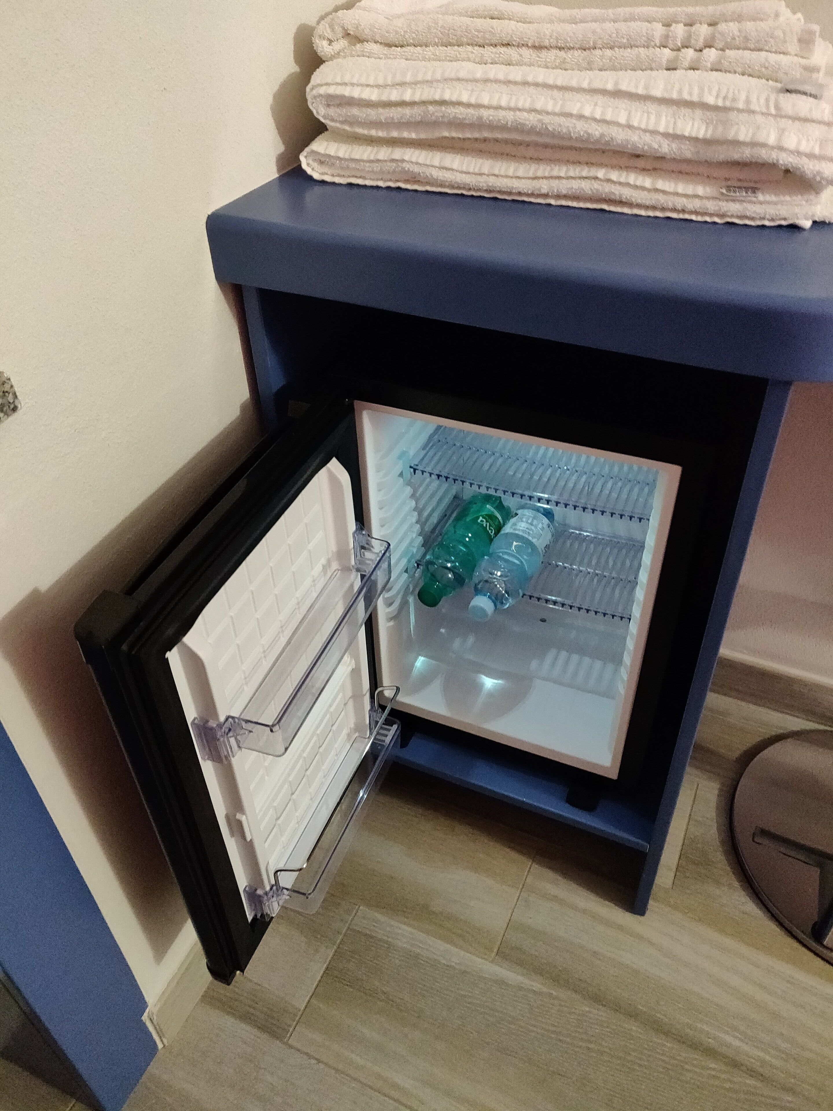 A compact refrigerator with a freezer compartment, containing water bottles and a folded towel on top.