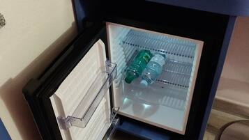 A compact refrigerator with a freezer compartment, containing water bottles and a folded towel on top.