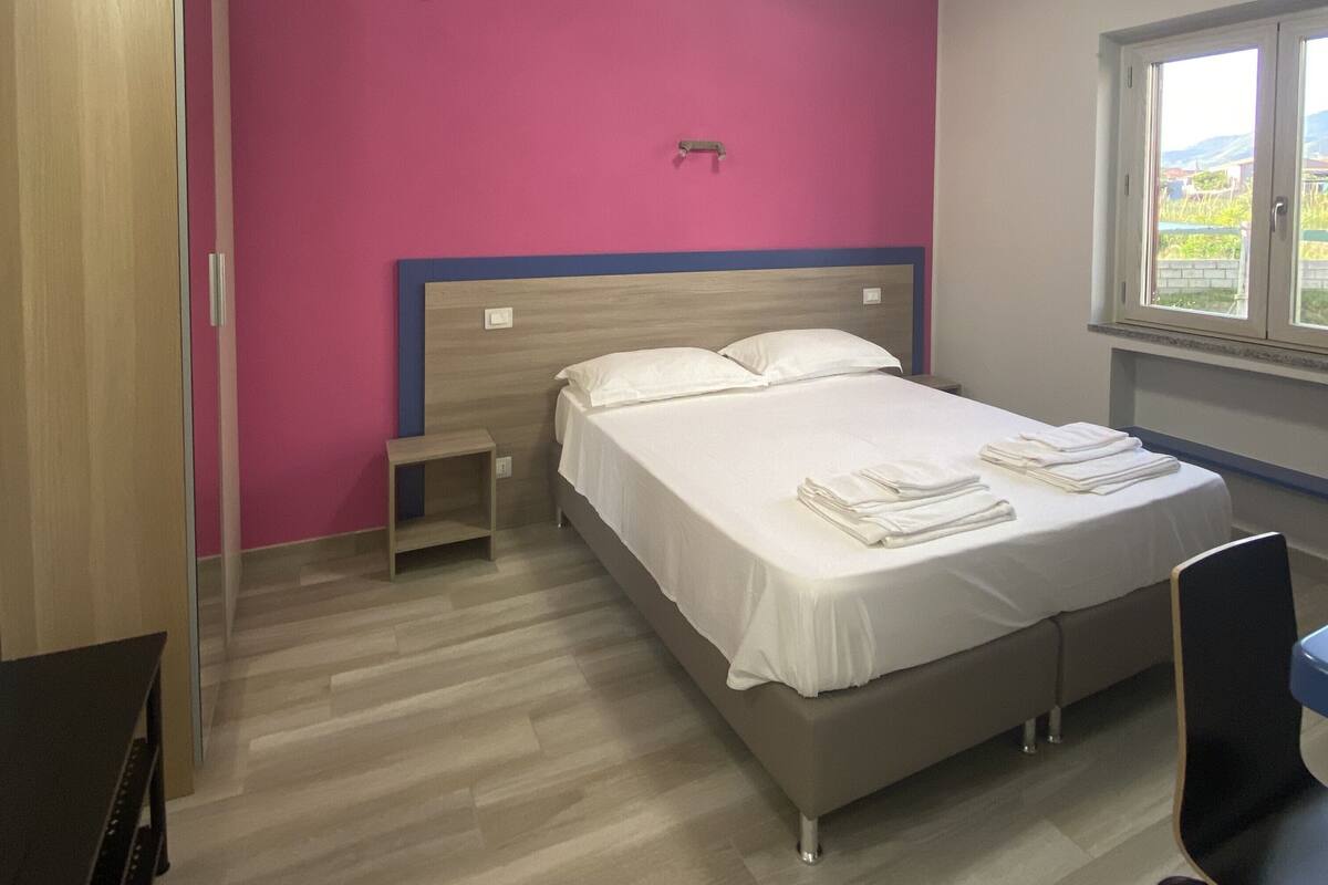 Une chambre à coucher comprenant un lit, une table de chevet, une armoire en bois et une fenêtre donnant sur un beau paysage.