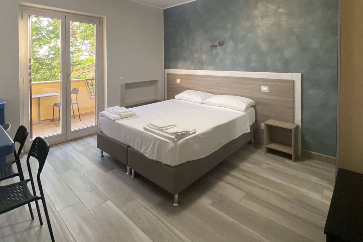 Une chambre à coucher comprenant un lit, une table de chevet, une chaise, un bureau et un balcon avec une table et des chaises.