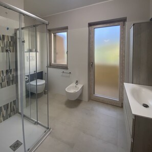 Un baño moderno con cabina de ducha de vidrio, inodoro, bidé y lavamanos.