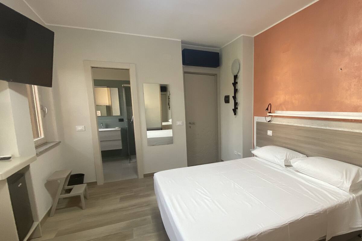 Une chambre à coucher avec un lit, un téléviseur fixé au mur, un plancher en bois et une porte donnant sur une salle de bain.