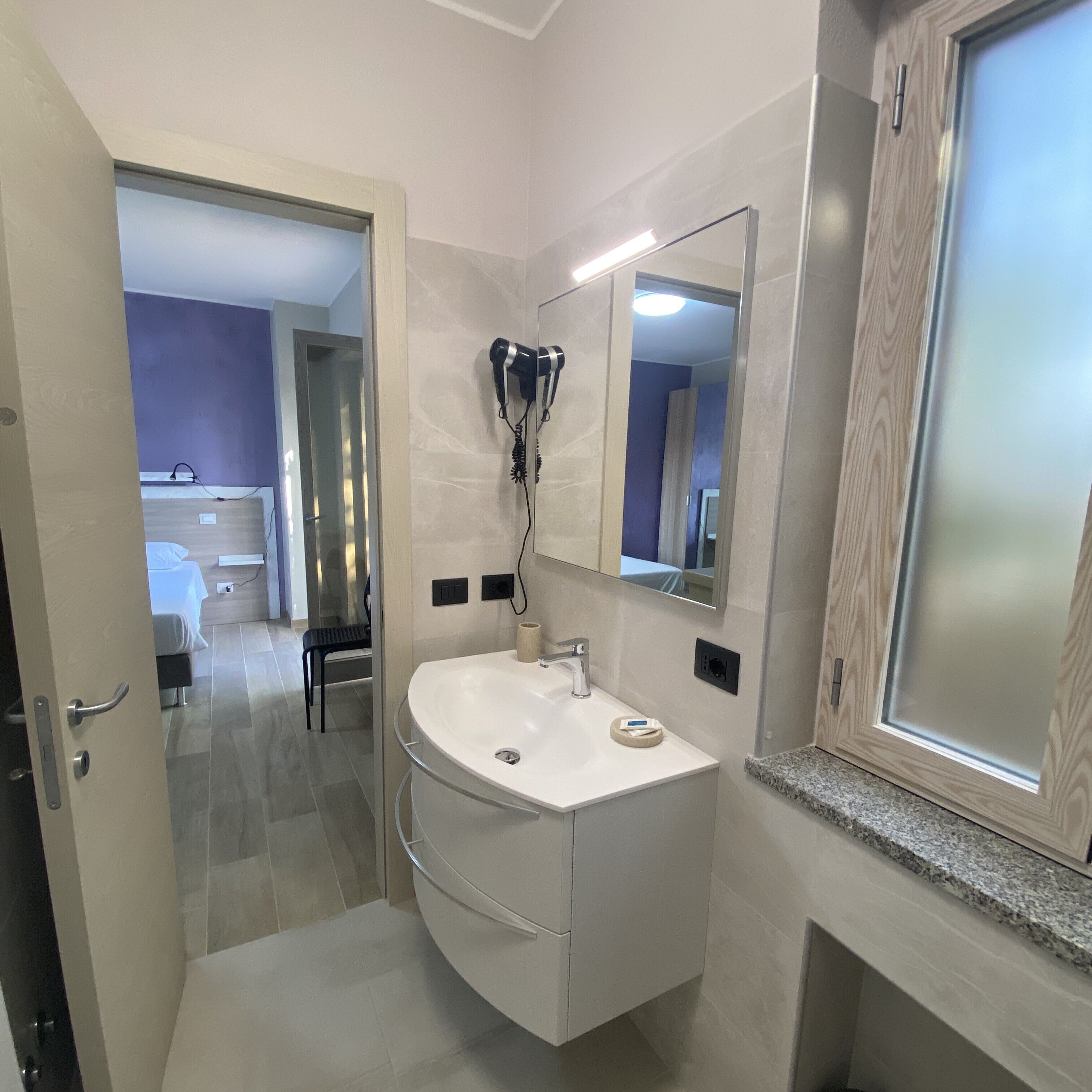 Un baño moderno con un lavabo blanco, un secador de pelo montado en la pared y un espejo sobre el lavabo.
