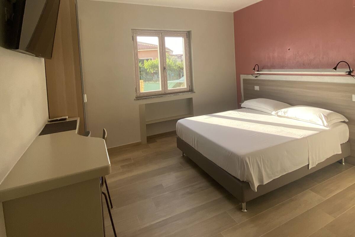 Une chambre à coucher avec un lit, un bureau, une fenêtre et un luminaire au plafond.