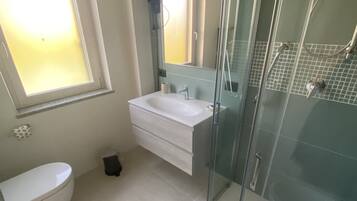 Een badkamer met een douchecabine, een wit wastafelmeubel en een toilet.