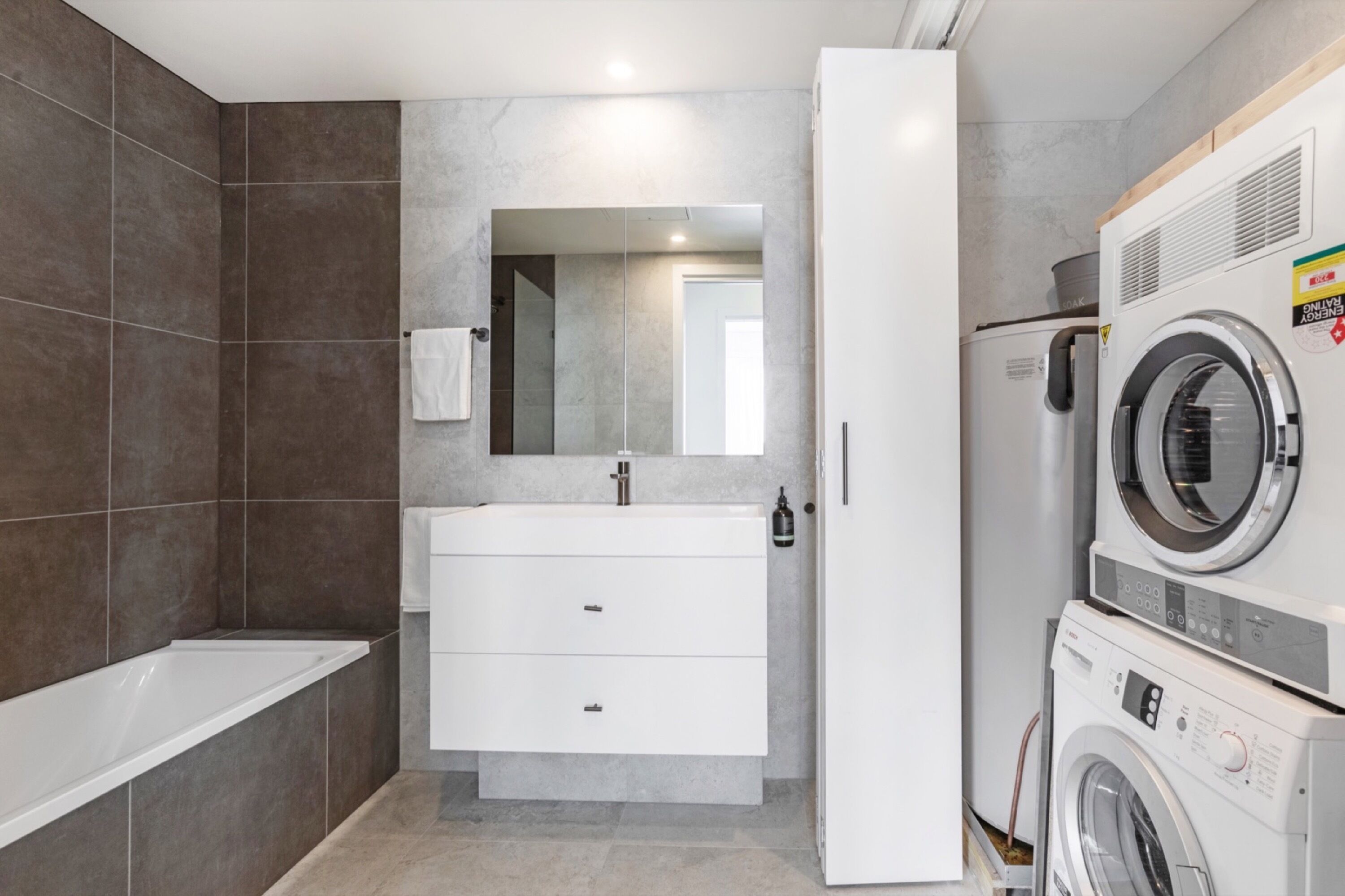 A modern bathroom with a bathtub, a vanity with a mirror, and a stacked washer and dryer.