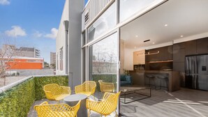 Um pátio externo com cadeiras amarelas e uma mesa, uma cozinha moderna com armários escuros e vista para a cidade.