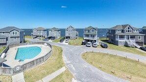 A coastal residential area with multiple two-story houses, a swimming pool, and a clear view of the sea.