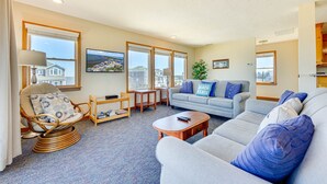 A spacious living room with a large window, a comfortable sofa, a reading chair, and a small table.
