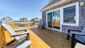 A wooden deck with chairs and a table, overlooking a residential area with houses and a body of water.