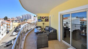 Ein Balkon mit Korbmöbeln, einer Glastür und Blick auf die Stadtlandschaft.