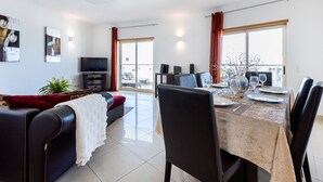 Ein modernes Wohnzimmer mit Sofa, Fernseher und Essbereich mit Stühlen und Tisch.