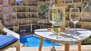 Ein Tisch mit einer Weinflasche und einem Glas, mit Blick auf einen Pool und ein Gebäude mit Balkonen.