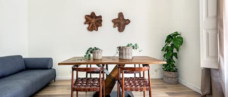 A dining area with a wooden table and chairs, two wall-mounted decorations, a blue sofa, and a potted plant.