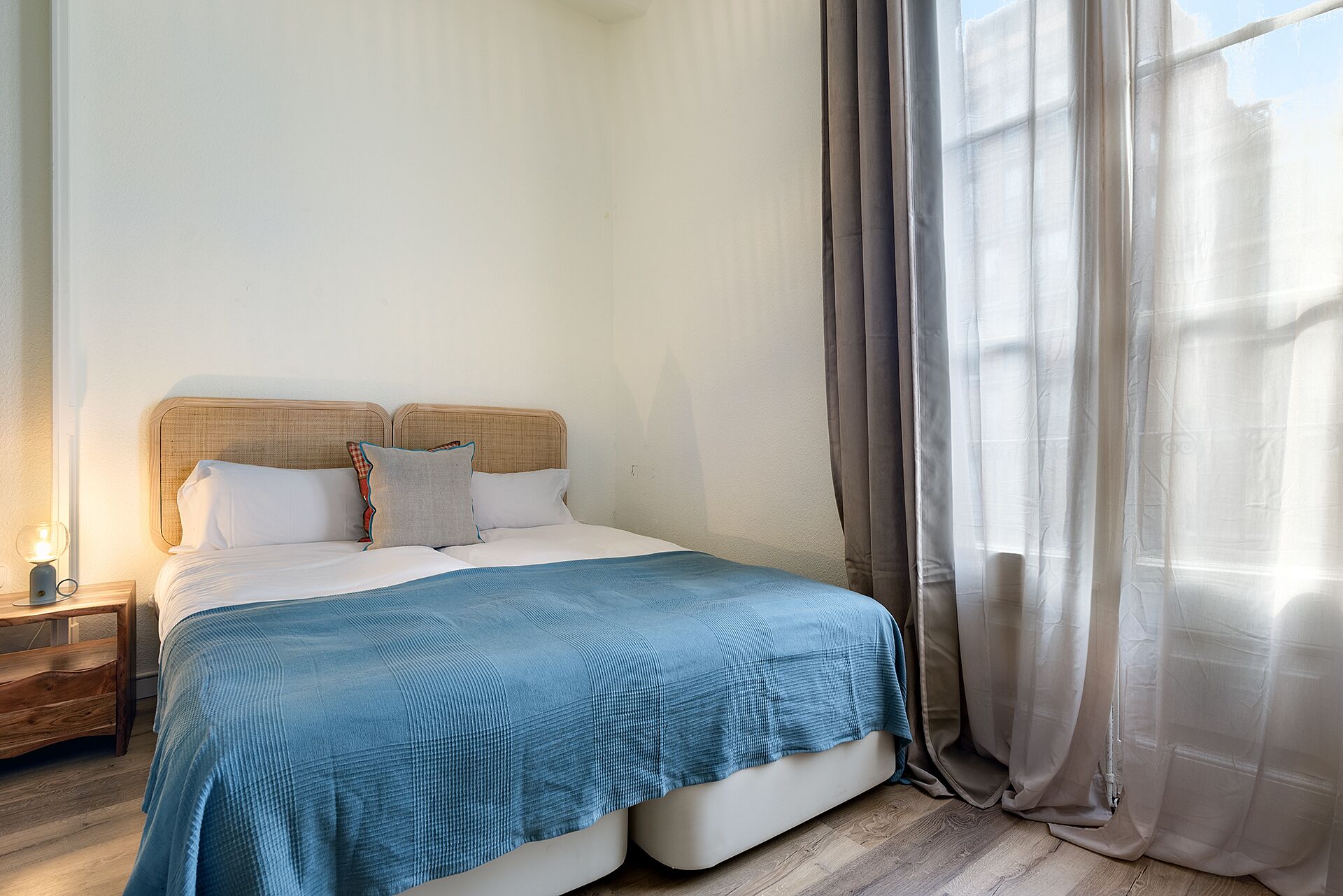 A bedroom with a bed, a nightstand, and a window with curtains.