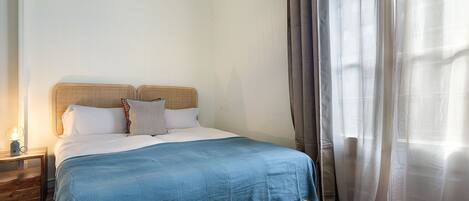 A bedroom with a bed, a nightstand, and a window with curtains.
