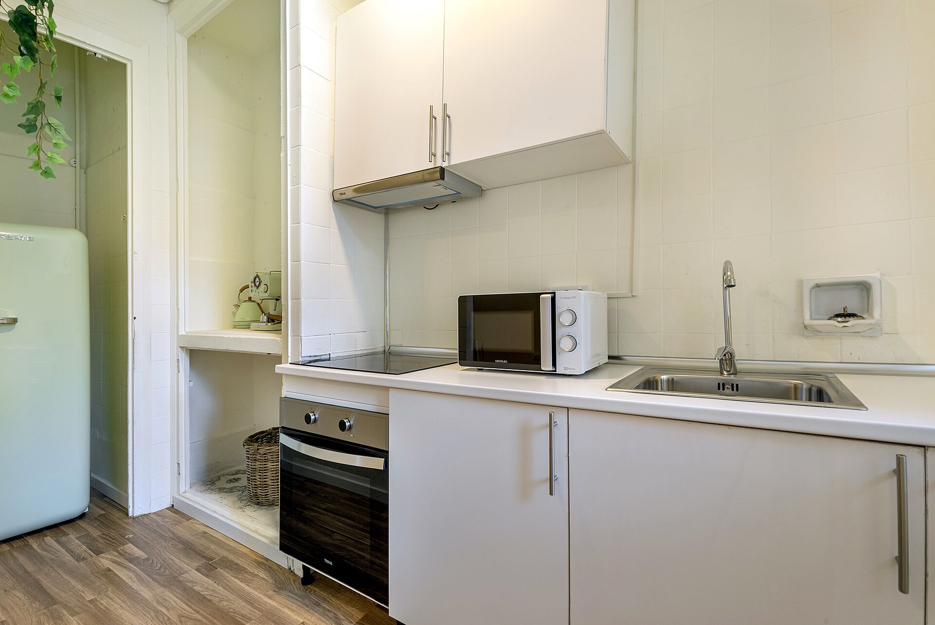 Una cucina compatta con mobili bianchi, un forno a microonde, un lavello e un frigorifero.