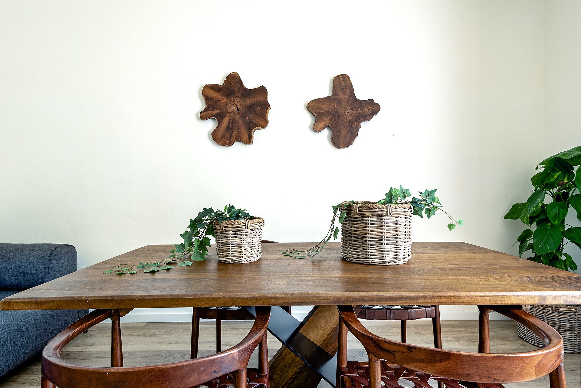 A wooden dining table with two wicker baskets containing green plants, surrounded by wooden chairs.