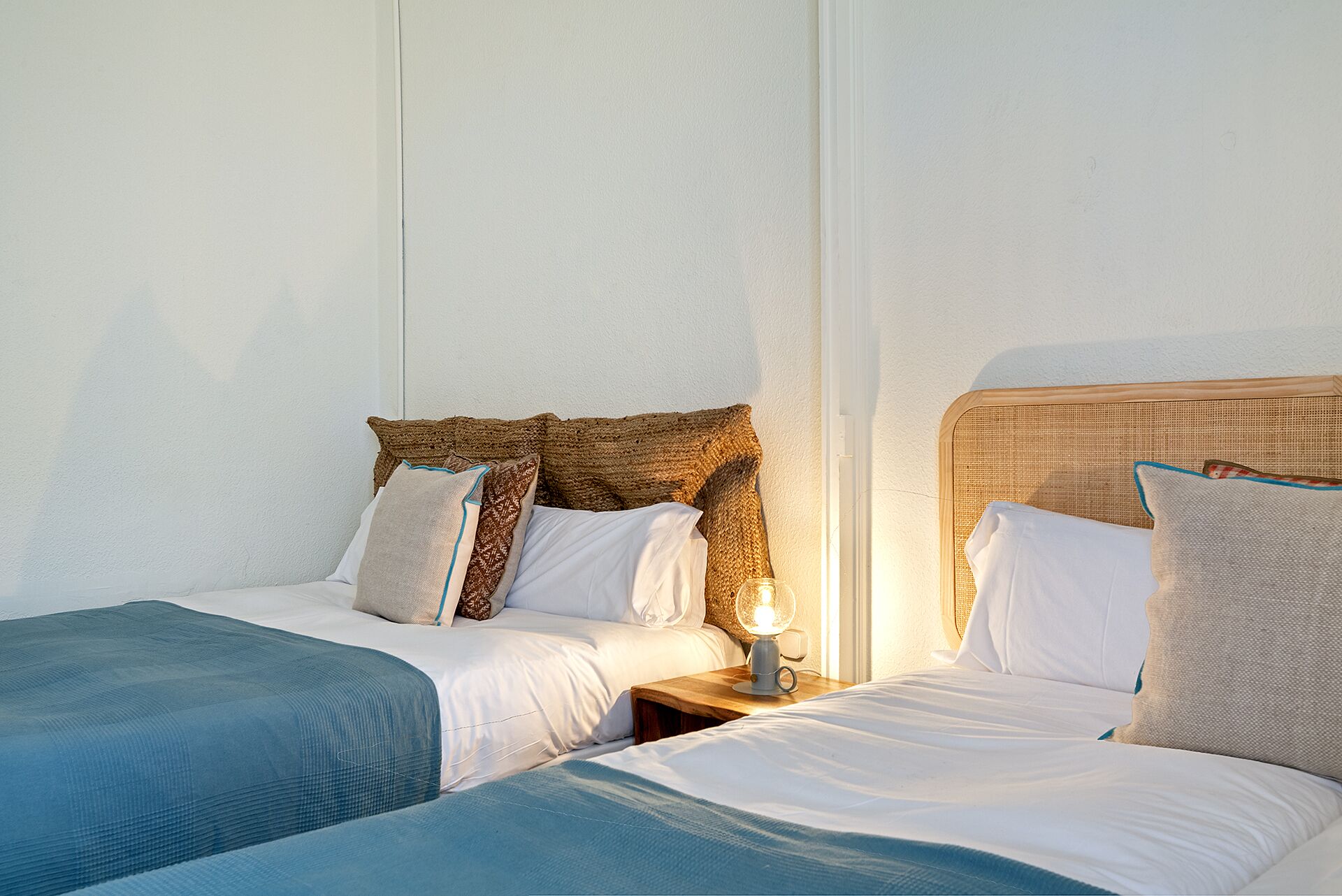 A hotel room with two single beds, each with a wooden headboard, white bedding, and a small bedside table with a lamp.