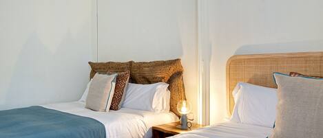 A hotel room with two single beds, each with a wooden headboard, white bedding, and a small bedside table with a lamp.