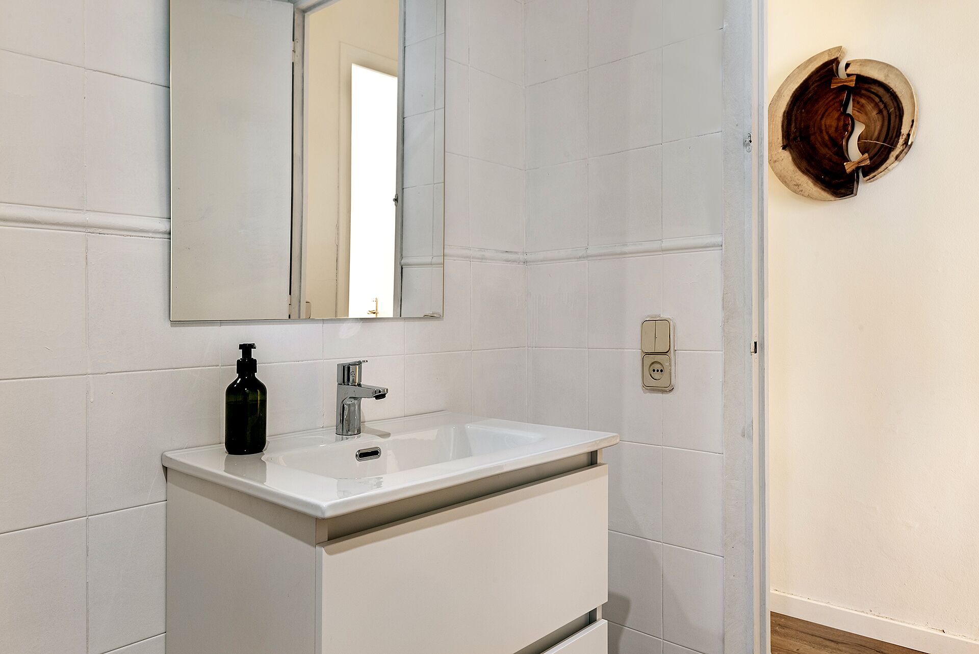 A bathroom with a white sink, a mirror, and a wooden wall decoration.