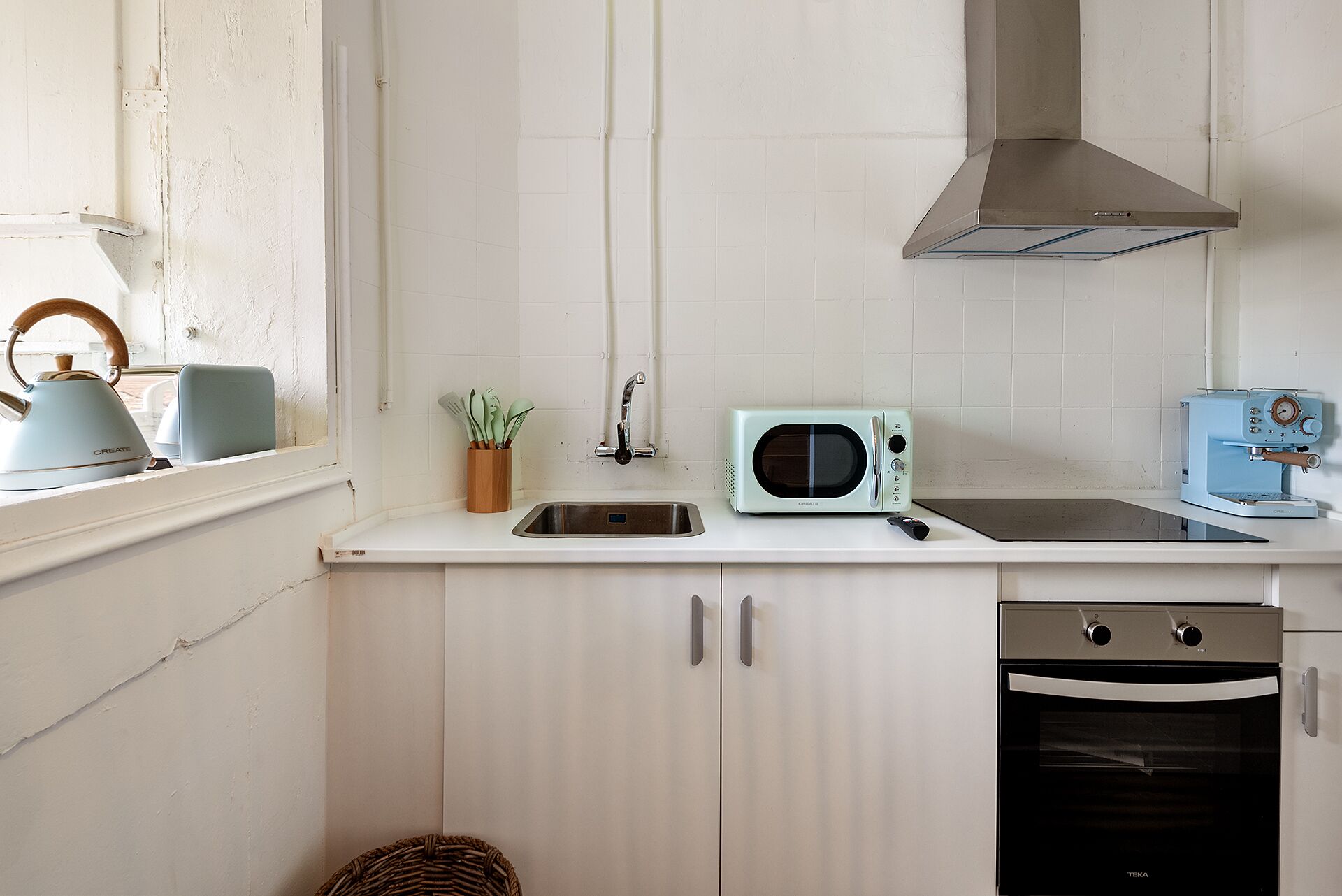 Une cuisine compacte avec des meubles blancs, un four à micro-ondes, une bouilloire et un lave-vaisselle.