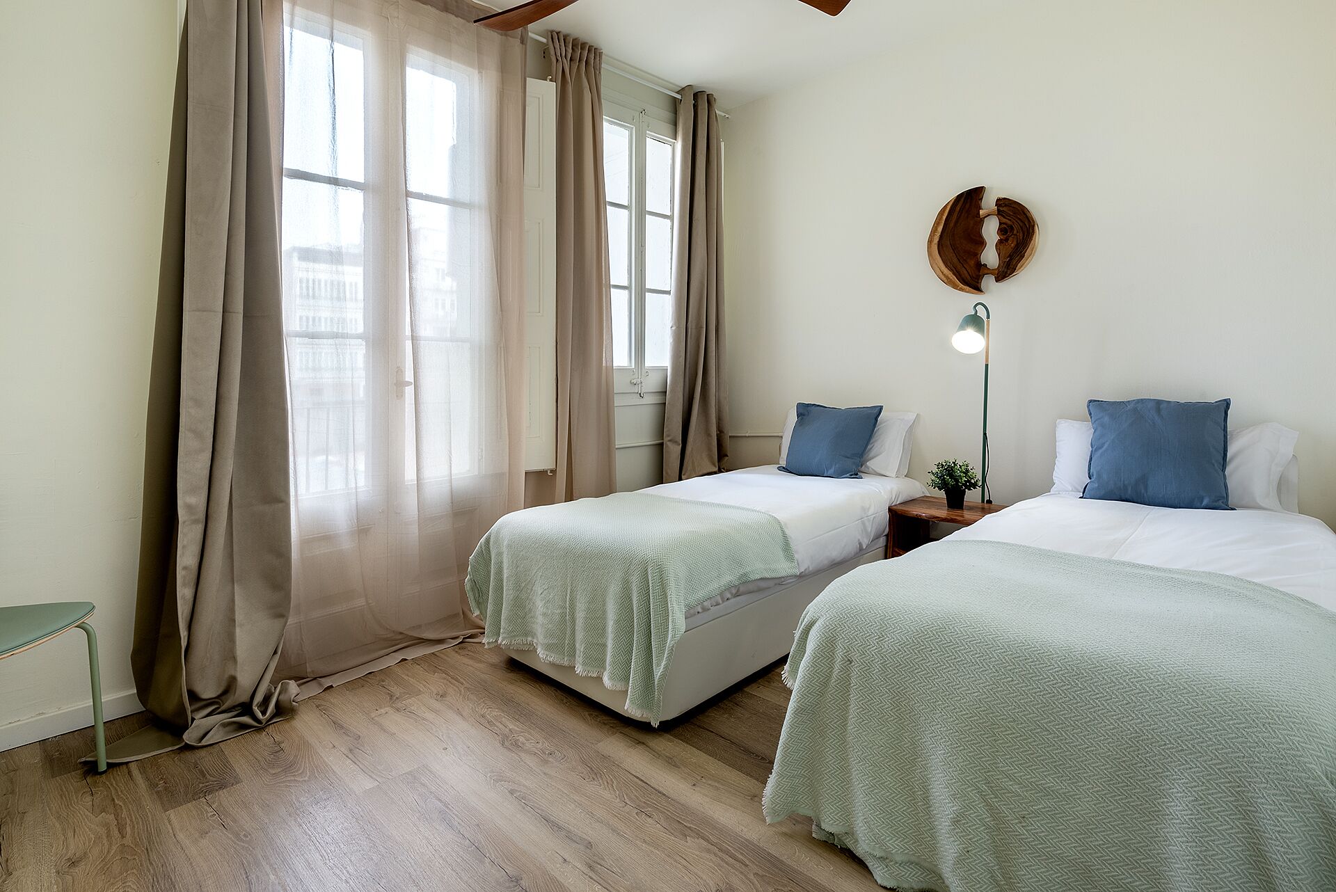 Een kamer met twee bedden, een bureau, een lamp en een raam met gordijnen.