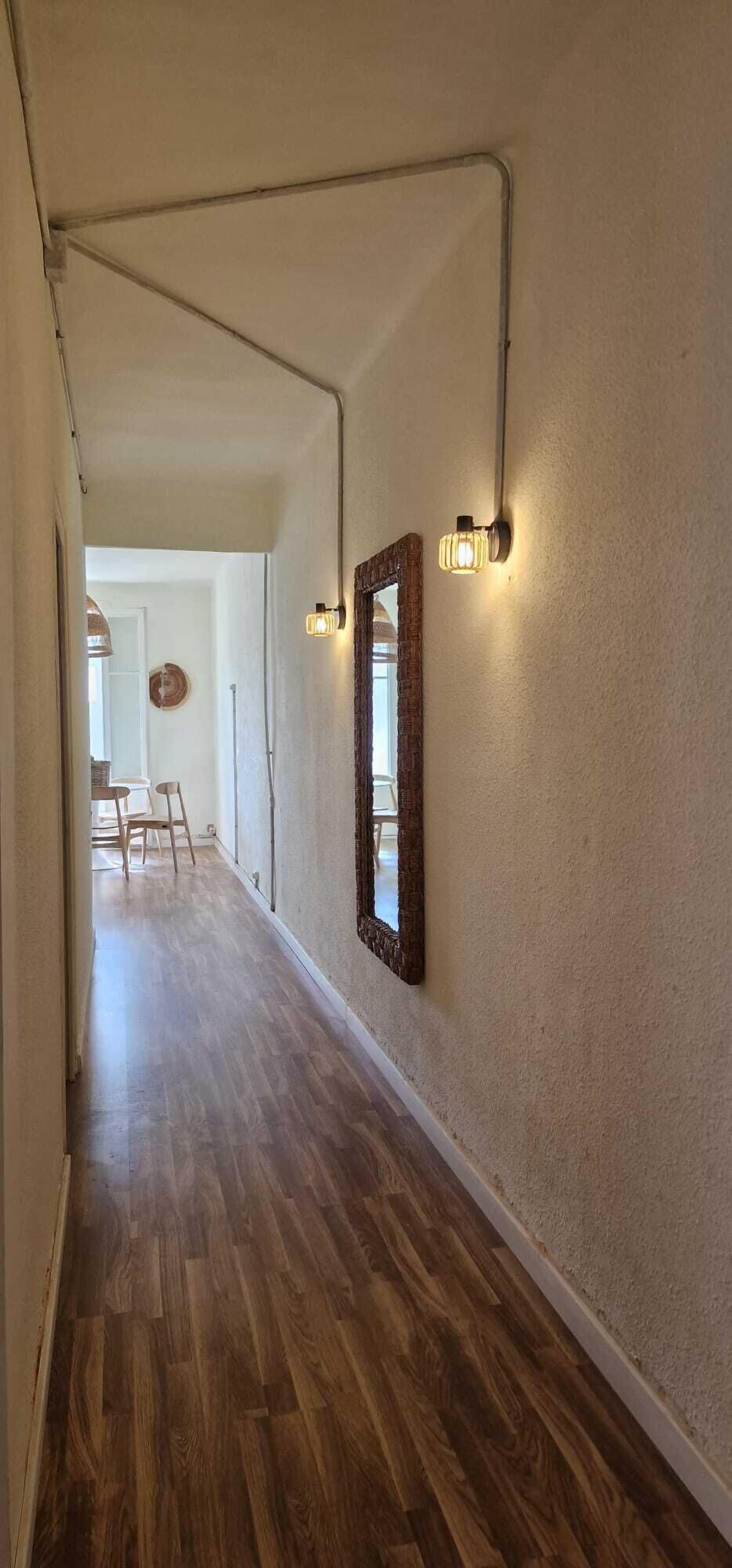A hallway with wooden flooring, a wall-mounted mirror, and two wall sconces.