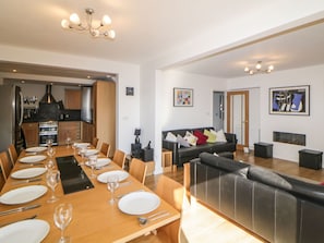 A spacious dining area with a long wooden table set for a meal, a black leather sofa, and a kitchen in the background.