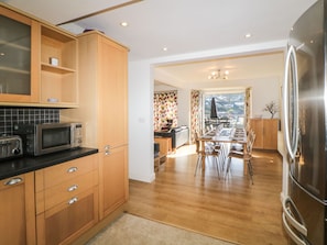 A modern kitchen with wooden cabinets, a stainless steel refrigerator, and a dining area with a view.