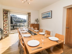 A dining area with a long wooden table set for six, a view of a balcony, and a framed picture on the wall.