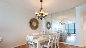 Uma sala de jantar com mesa e cadeiras de madeira, um candelabro e dois espelhos na parede.