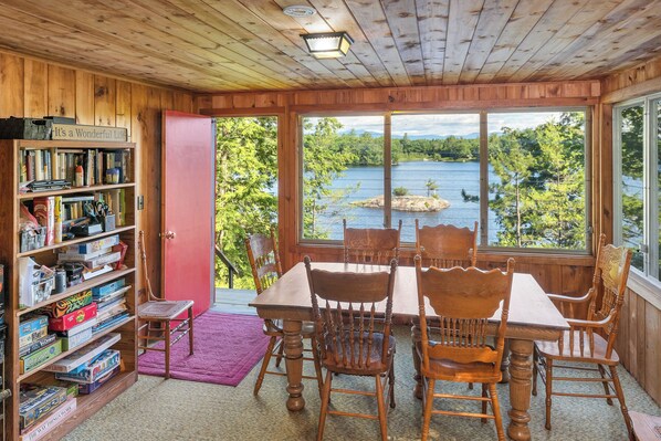 Un interno in legno con un tavolo e sedie, una libreria e vista su un lago attraverso ampie finestre.