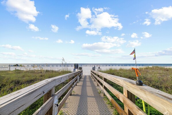 A wooden boardwalk leading to a beach with a flag on the right.