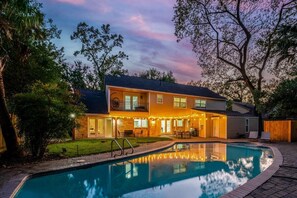 Una casa de dos plantas con piscina, iluminación exterior y un césped bien cuidado.