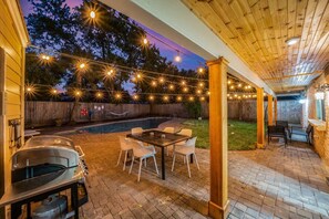 Un patio al aire libre con una parrilla, una mesa con sillas y luces colgantes.