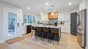 Una cocina moderna con armarios blancos, una isla central con taburetes y un refrigerador grande.