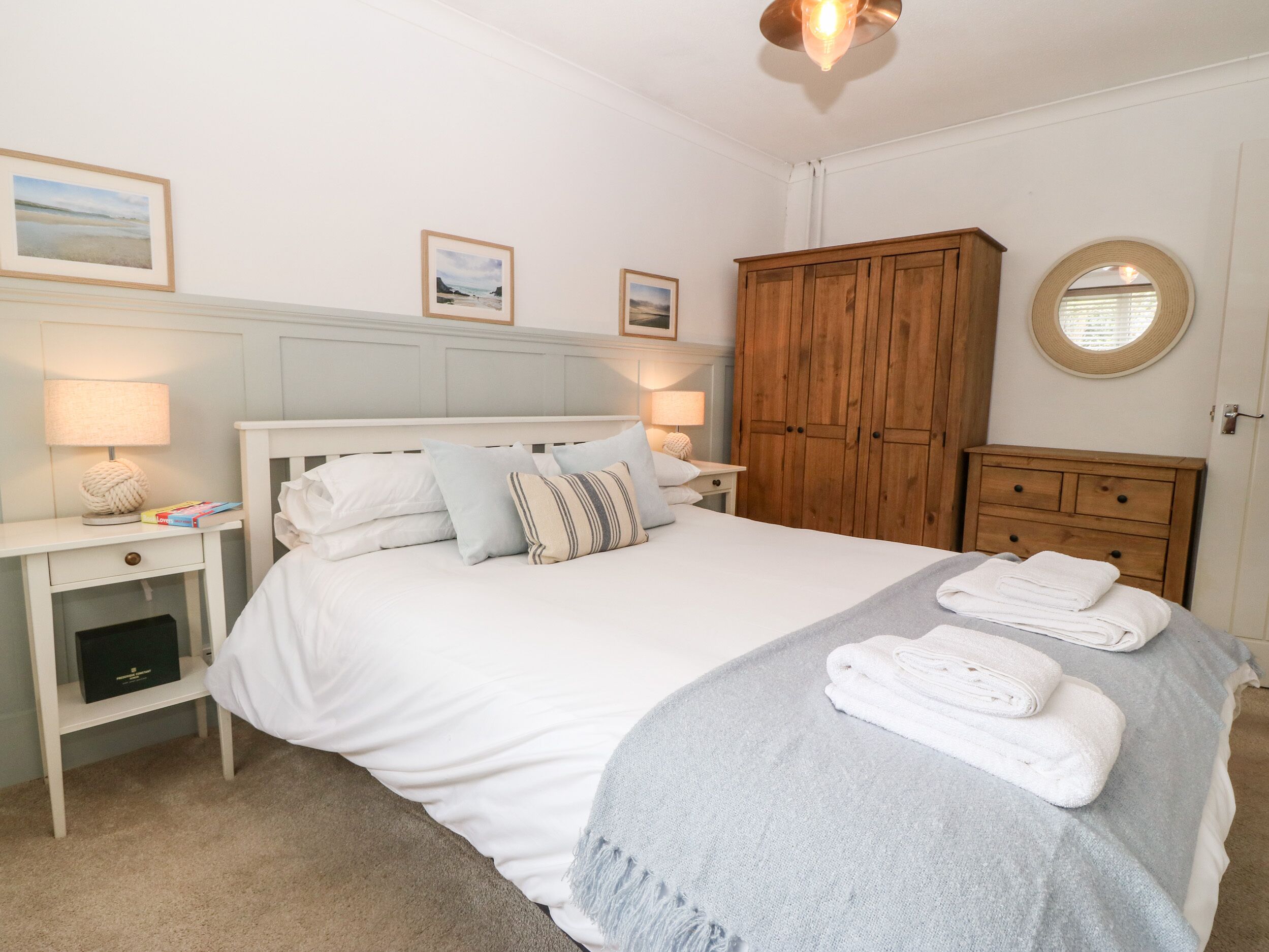 A neatly arranged bedroom with a bed, bedside tables, a wardrobe, and a round mirror.