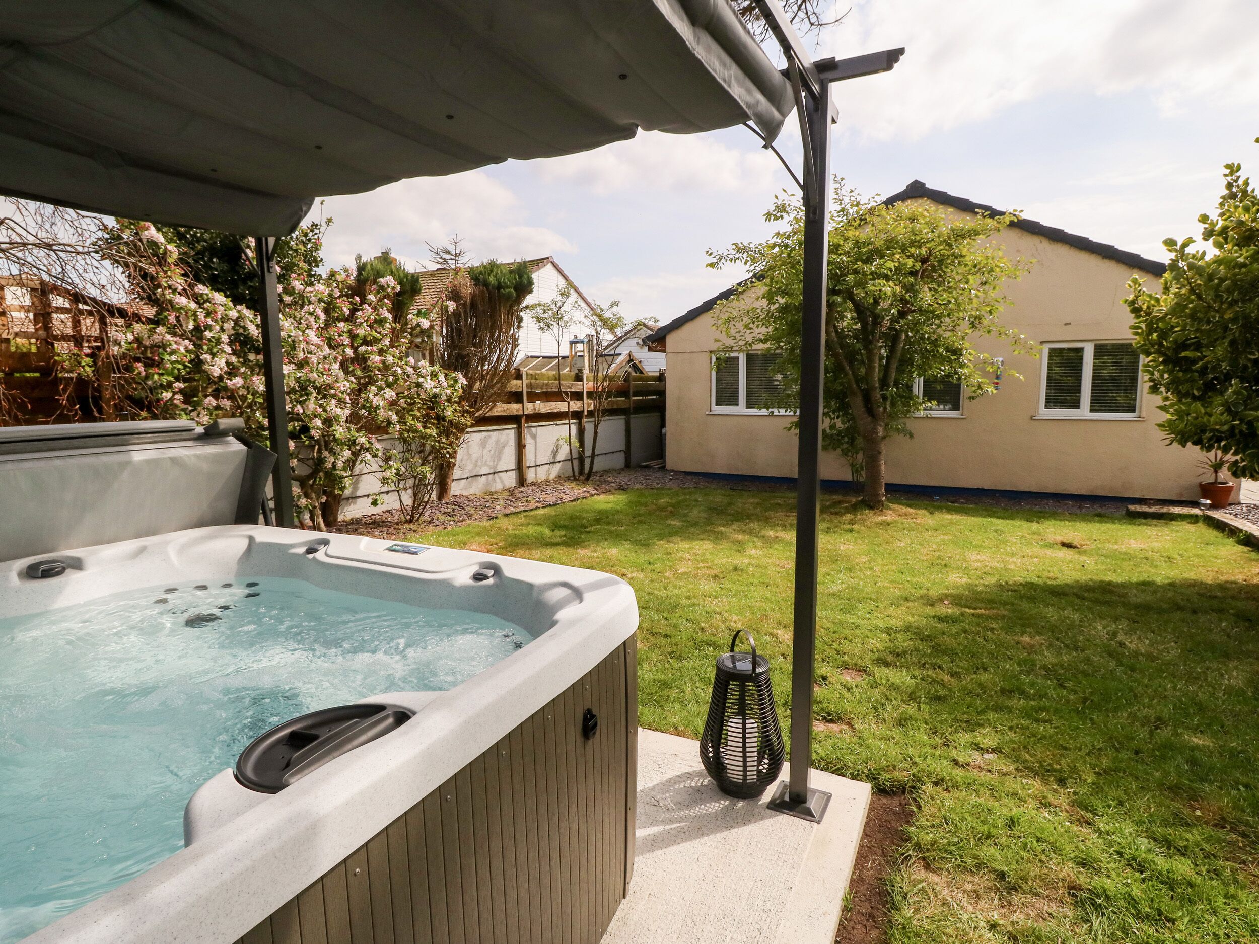 A backyard with a hot tub, a pergola, a potted plant, and a house in the background.